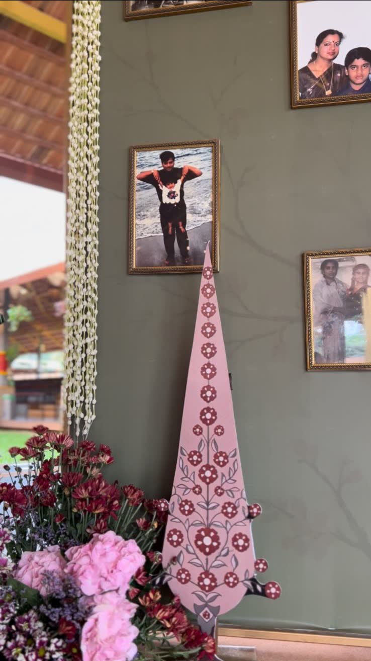 Close view of the painted kalash cutout with hanging jasmine ropes and framed family photographs on the sage green wall
