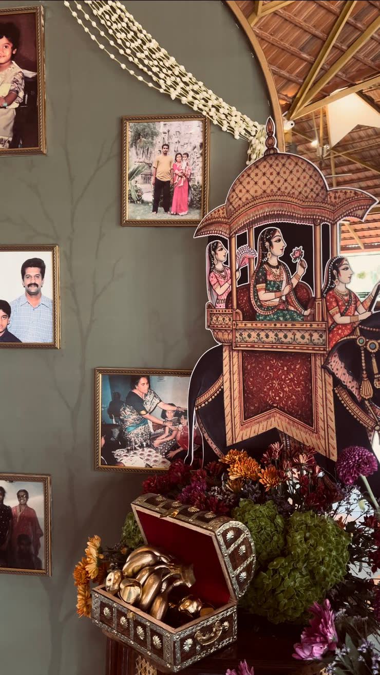 Painted kalash cutout in dusty pink with oxblood floral motif standing against the sage green arch beside jasmine ropes and chrysanthemum