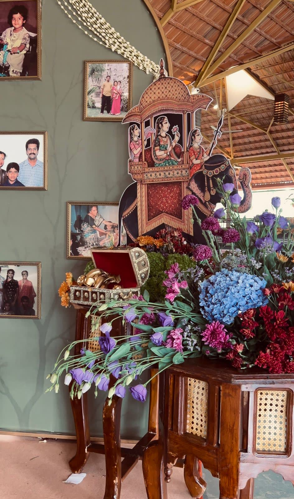 Painted Pichwai elephant and howdah cutout beside the family photograph arch with hydrangea, lisianthus and chrysanthemum on a carved wooden table