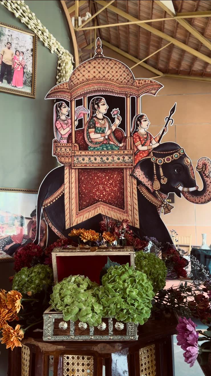 Detail of the Pichwai elephant cutout with an inlaid heirloom chest open at its base holding gold-painted fruit, framed by green hydrangea and chrysanthemum