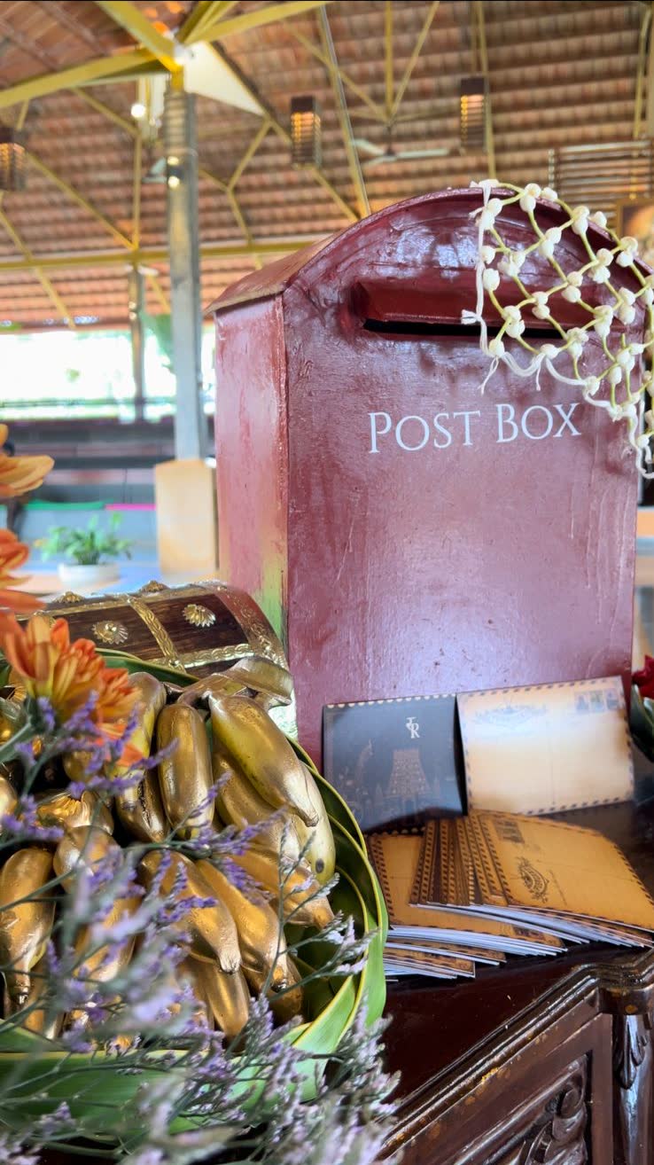 Close view of the painted post box with vintage-style postcards, an inlaid chest and gold-painted bananas on a folded leaf plate