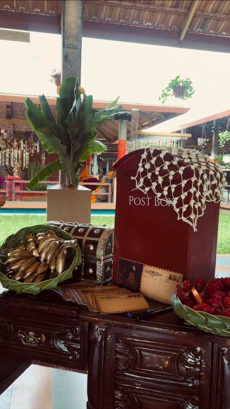 Red Indian Post letterbox on a carved teak desk with postcards and a hand-knotted jasmine net, banana plant behind, at Panchavati Pavilion