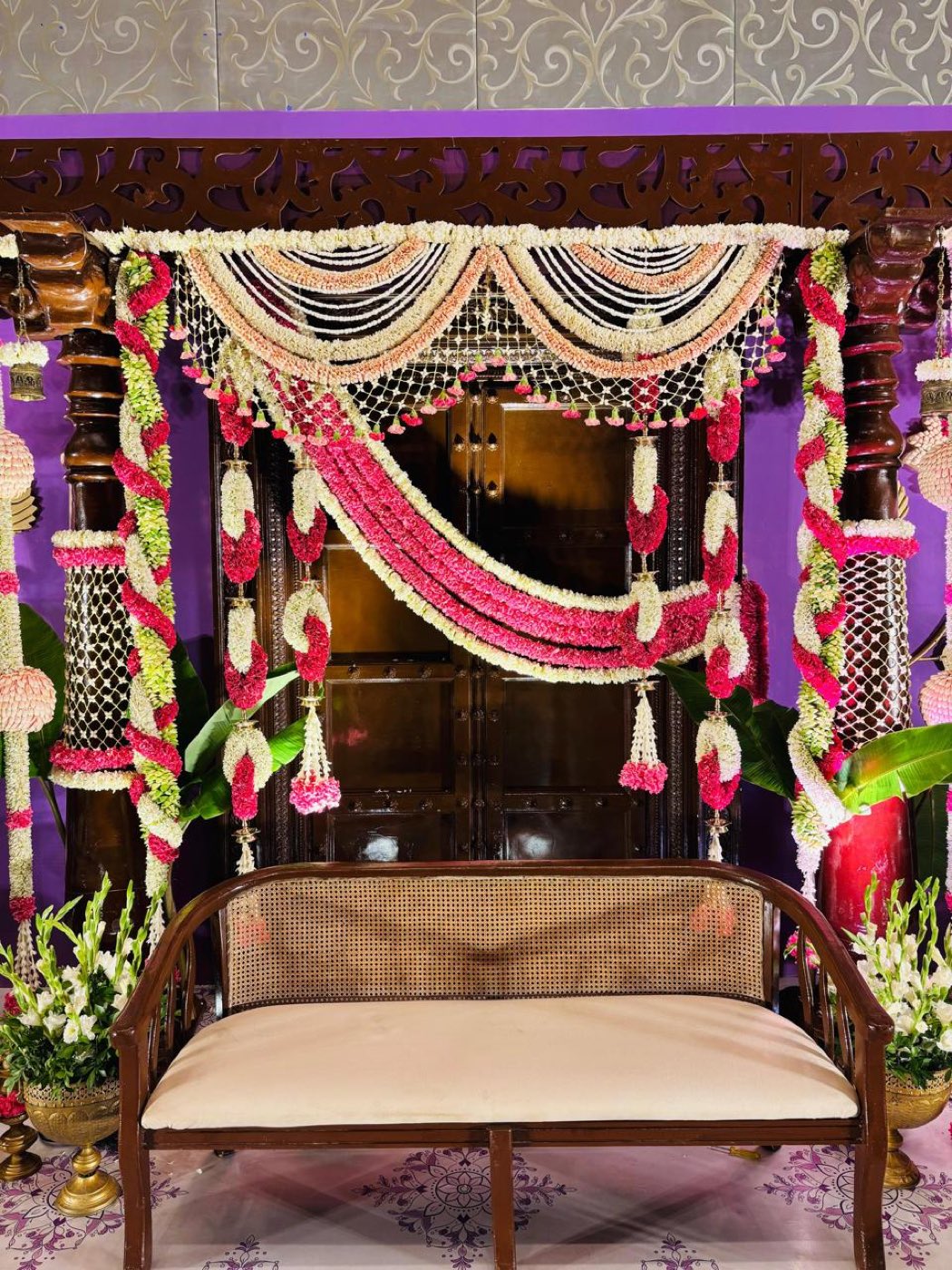 Carved cane bench seat under a jasmine and carnation swag on a purple backdrop at a half saree ceremony