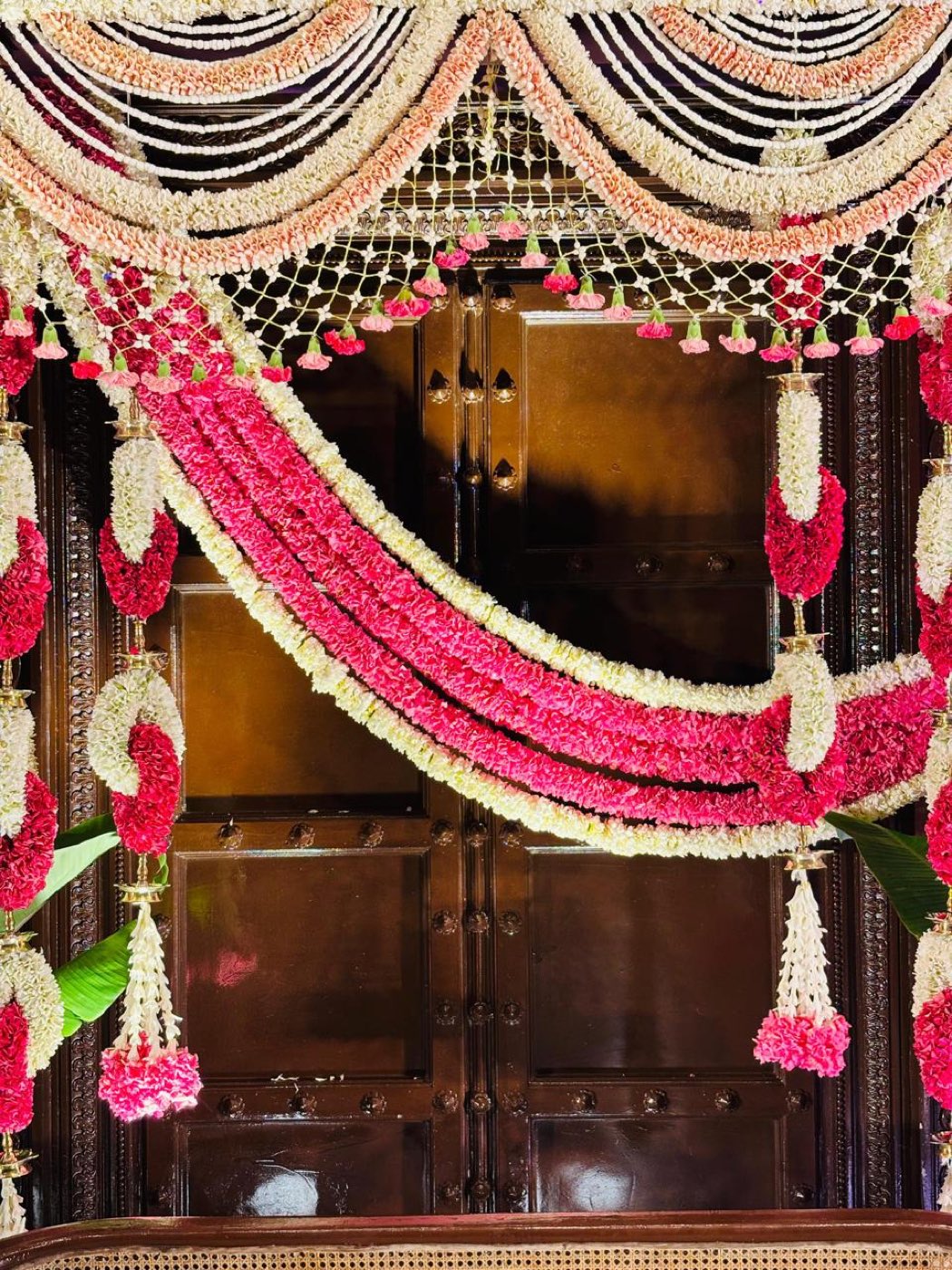 Close detail of graduated jasmine and carnation swags with a knotted net valance over a carved dark wood door