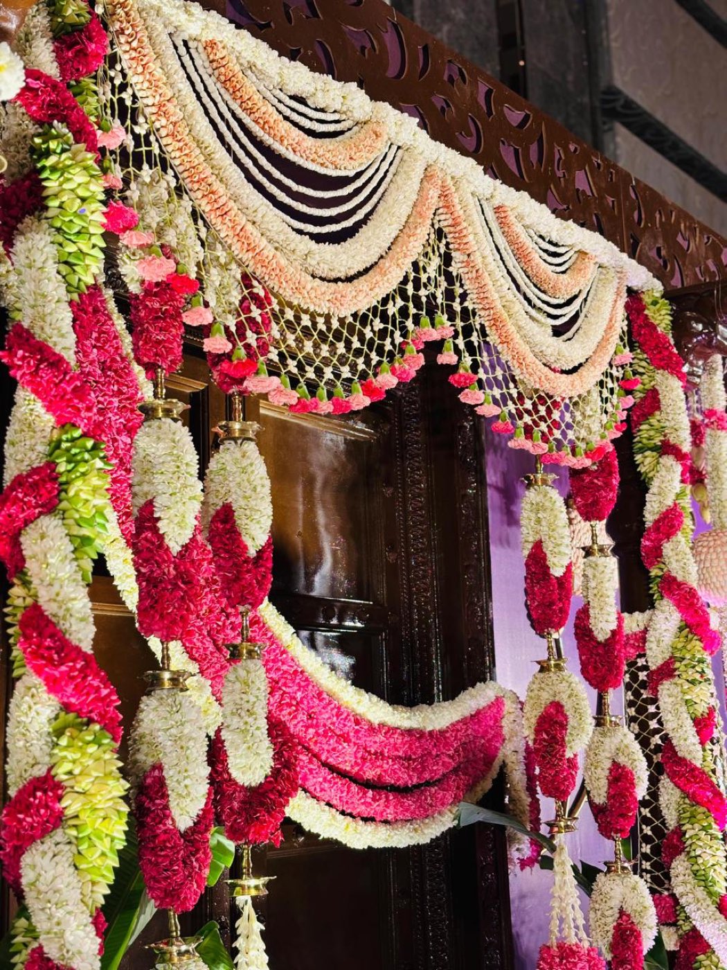 Braided jasmine and carnation rope columns framing the carved backdrop of a half saree ceremony stage
