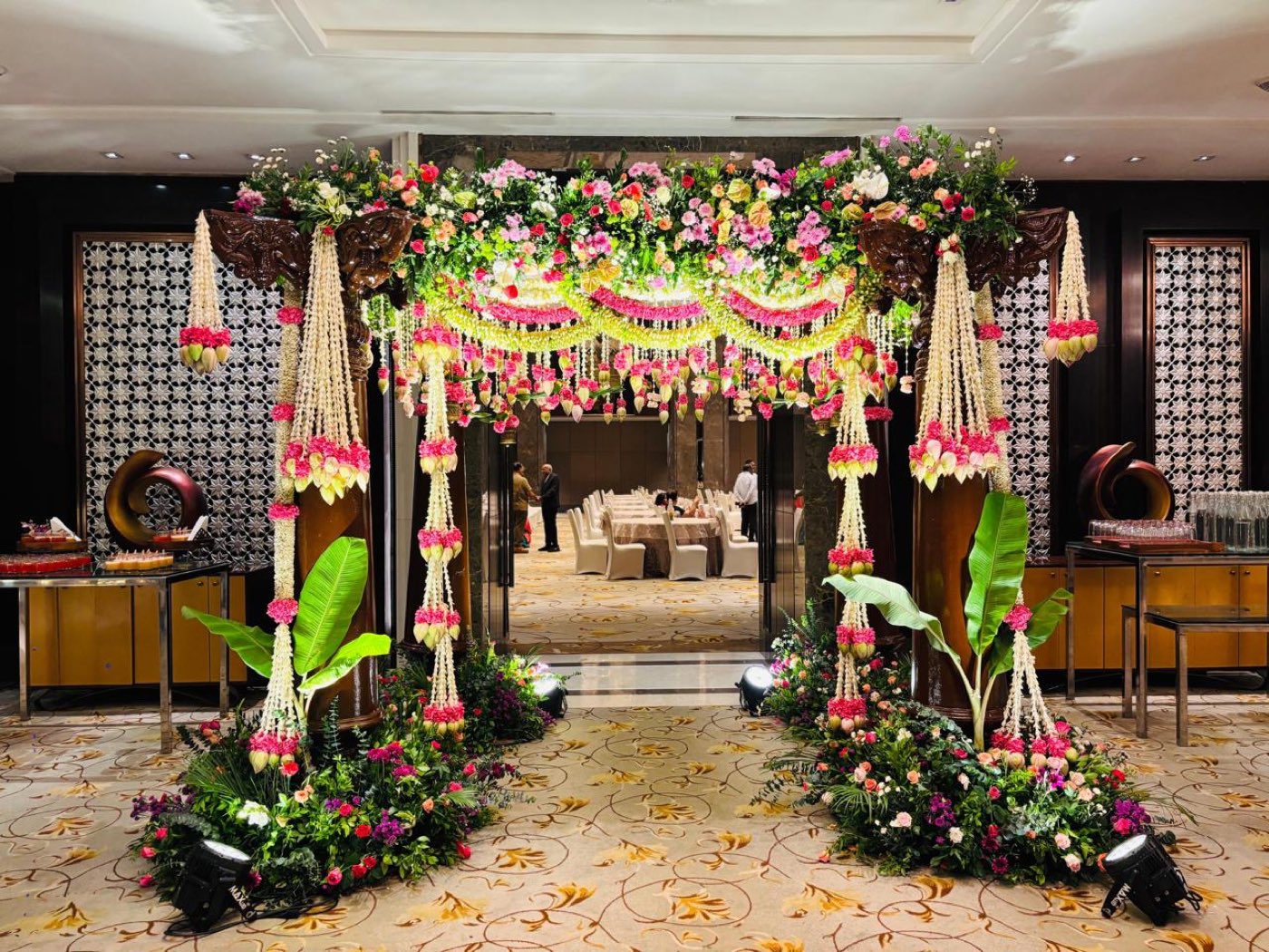 Floral entrance arch in pink and white with hanging garlands and banana leaf framing the Grand Ballroom doorway