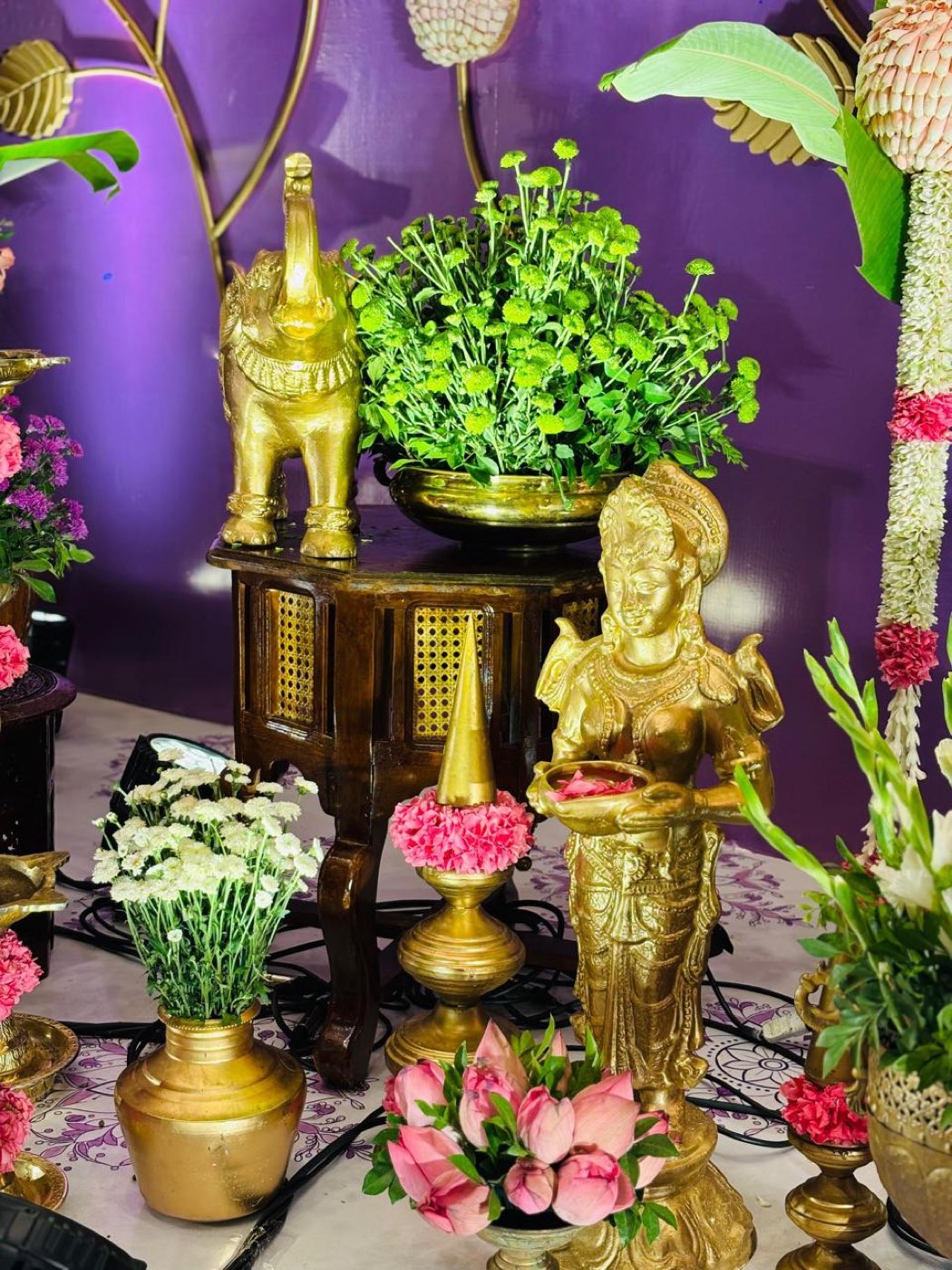 Brass deity figures, green chrysanthemum and lotus buds arranged on the half saree stage foreground