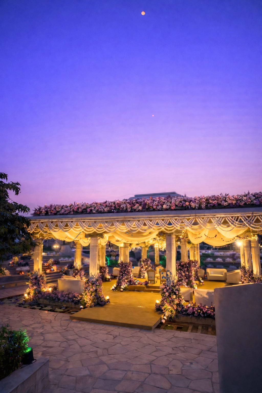 Illuminated wedding mantapa with floral roof and pearl swags under a purple evening sky at Amita Rasa, Nandi Hills near Bangalore