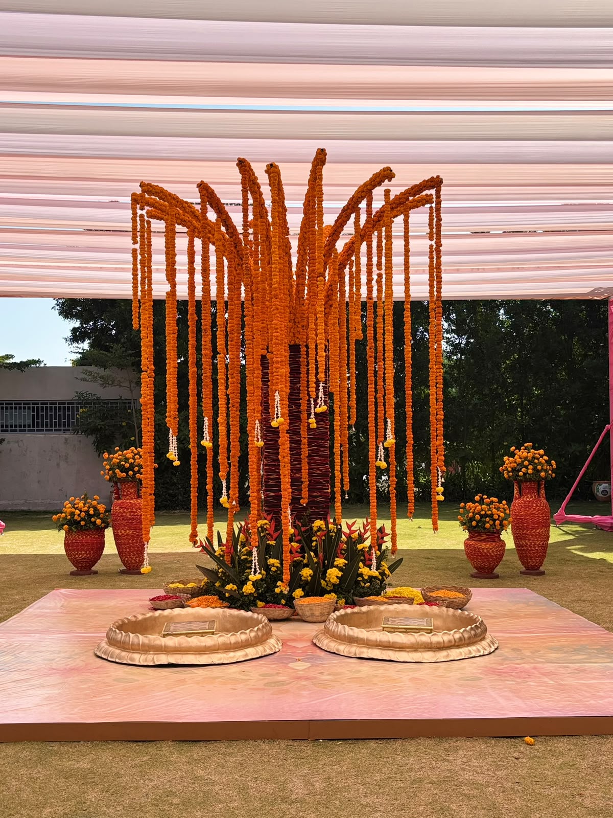 Haldi installation of marigold garland strands cascading from a central column over two gold basins at Amita Rasa, Nandi Hills near Bangalore