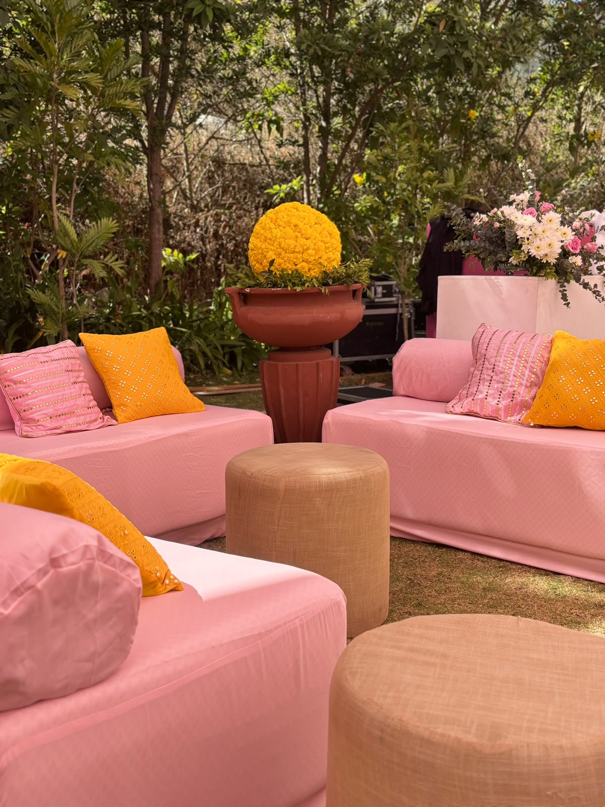 Pink floor lounge with yellow embroidered cushions and a marigold sphere in a terracotta urn under trees at Amita Rasa, Nandi Hills near Bangalore