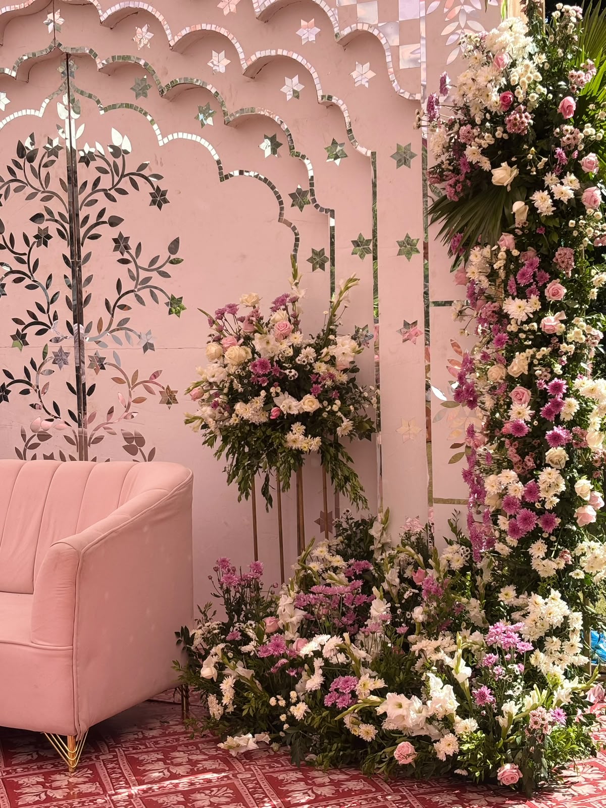 Detail of mirror-work leaf vines and stars on the pink jharokha backdrop with pink and white floral columns
