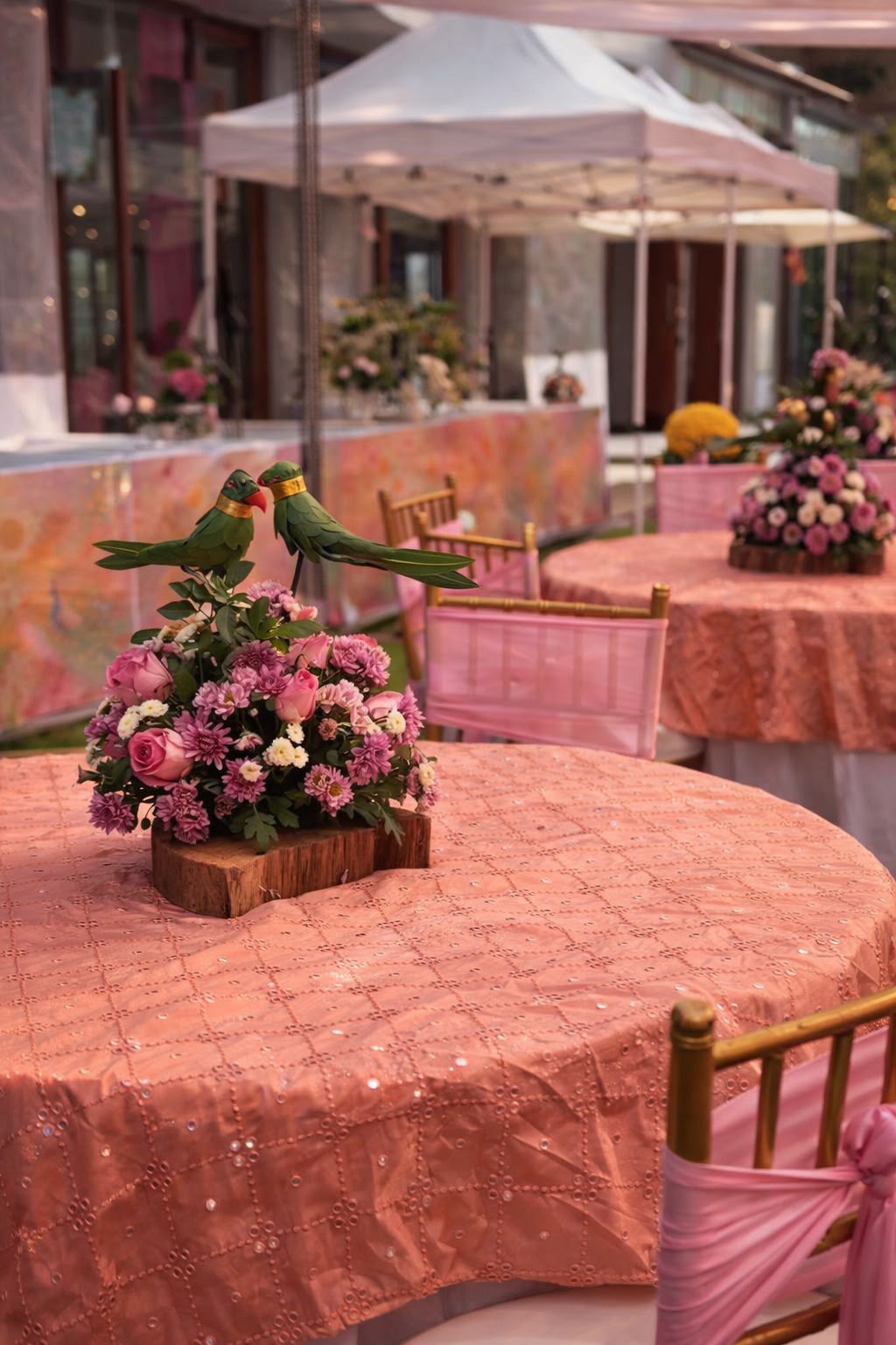 Green parrot figures over a pink floral centrepiece on mirror-embroidered rose pink tablecloth at a mehendi