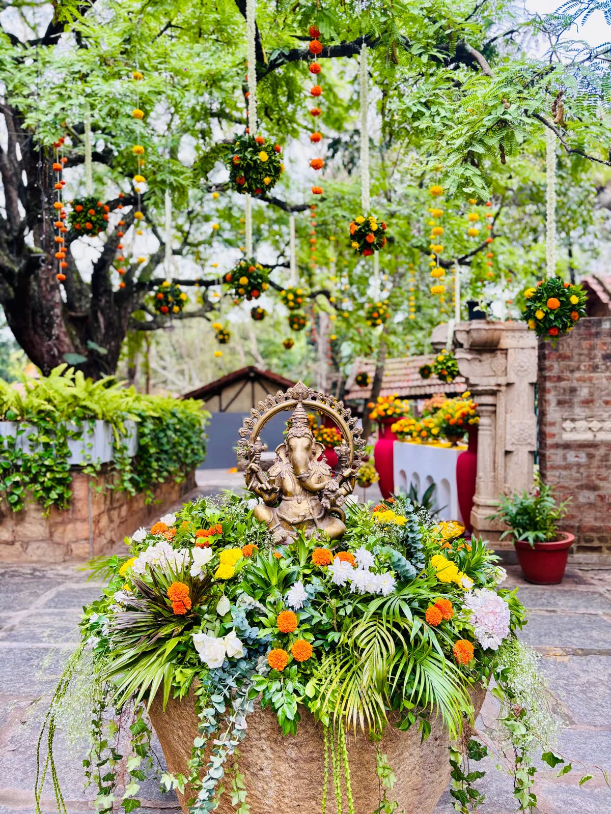 Brass Ganesha set in a stone urn filled with marigold, chrysanthemum, palm and trailing ivy, under the hanging marigold canopy