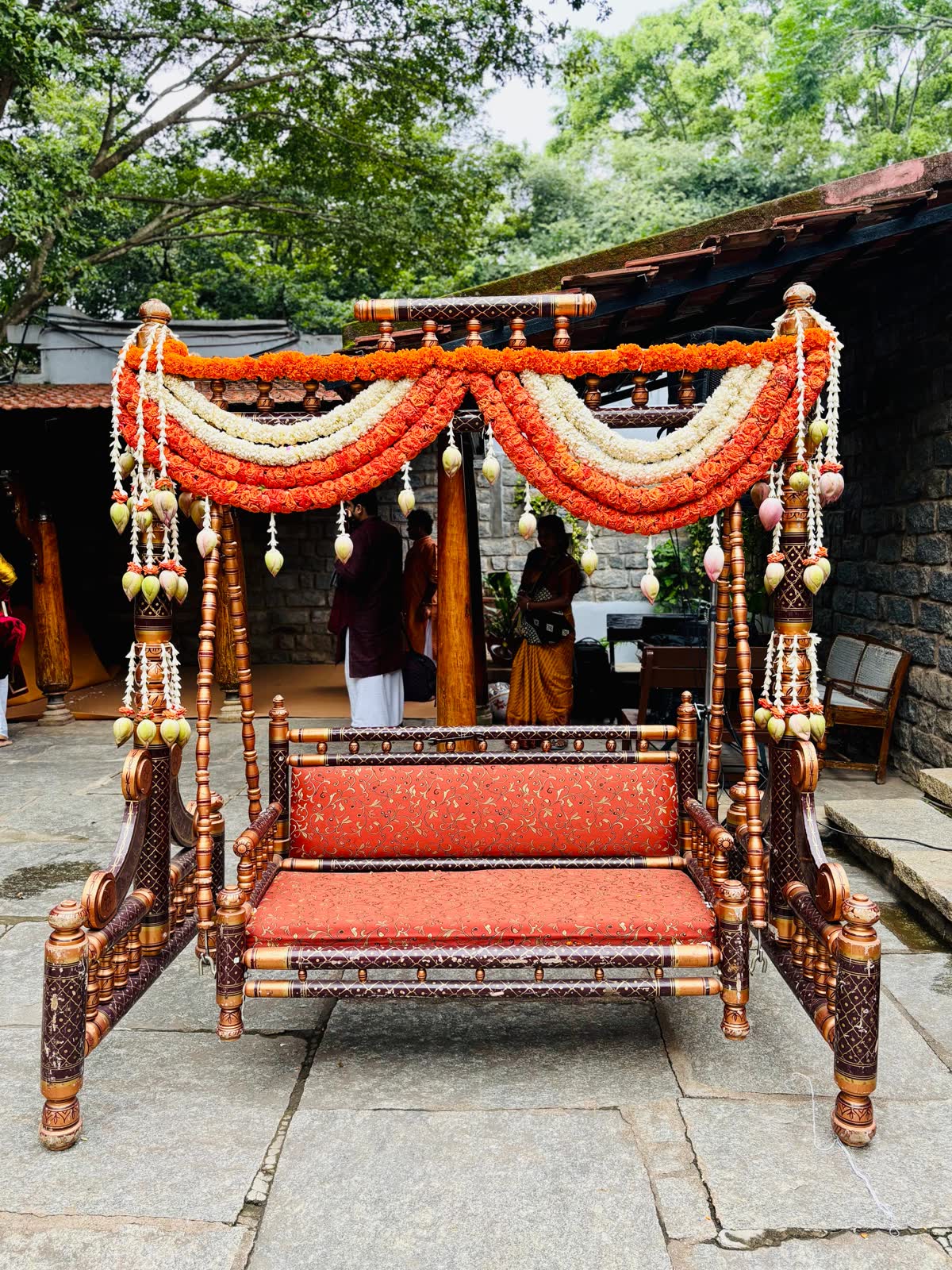 Traditional turned and lacquered jhoola swing seat with layered orange rose and white jasmine swags and lotus bud tassels at The Tamarind Tree