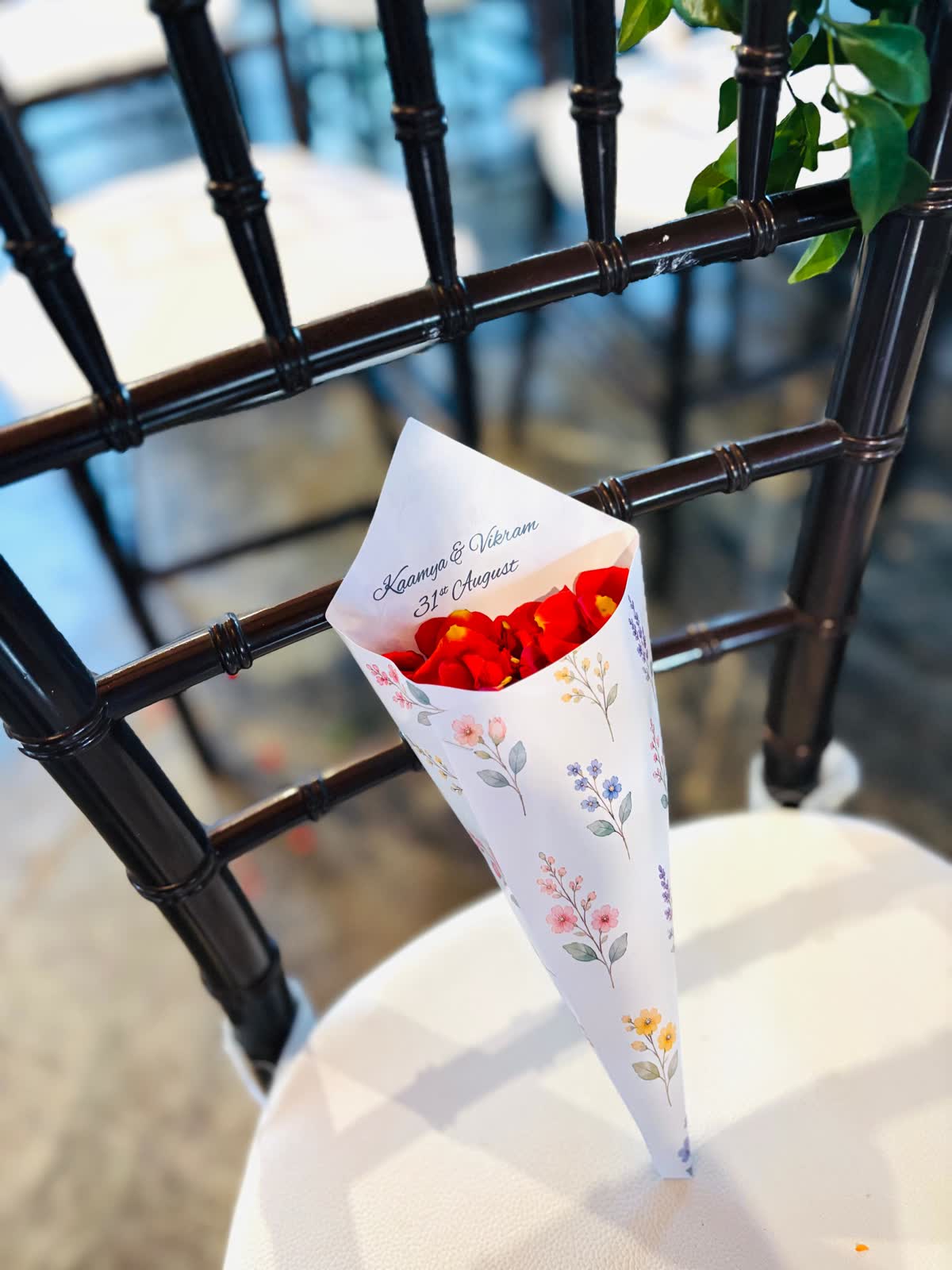 A single printed petal cone with a floral border resting on the cream cushion of a dark chiavari chair