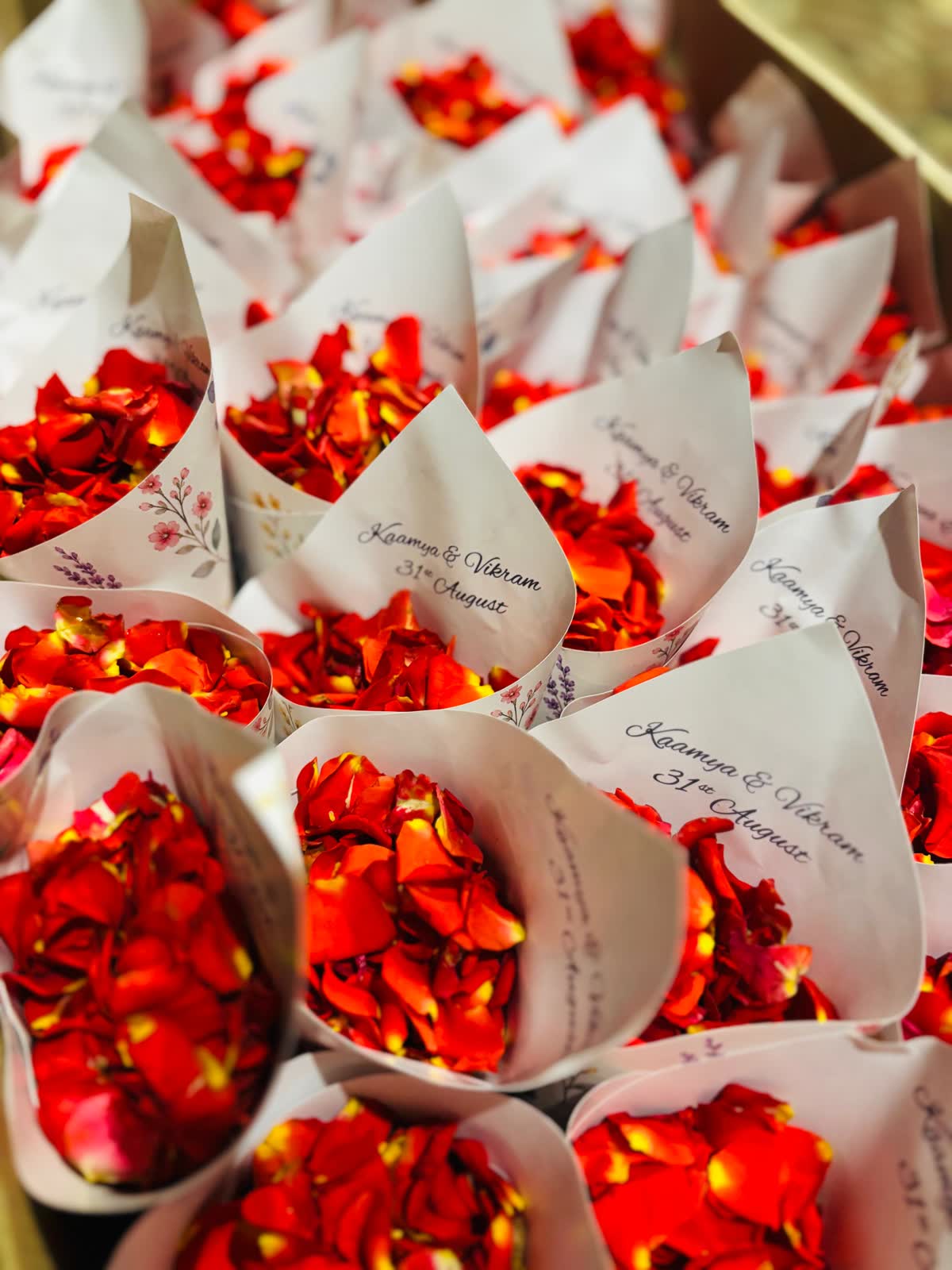 Trays of paper cones printed with Kaamya and Vikram 31st August, filled with red and orange rose petals for the wedding procession