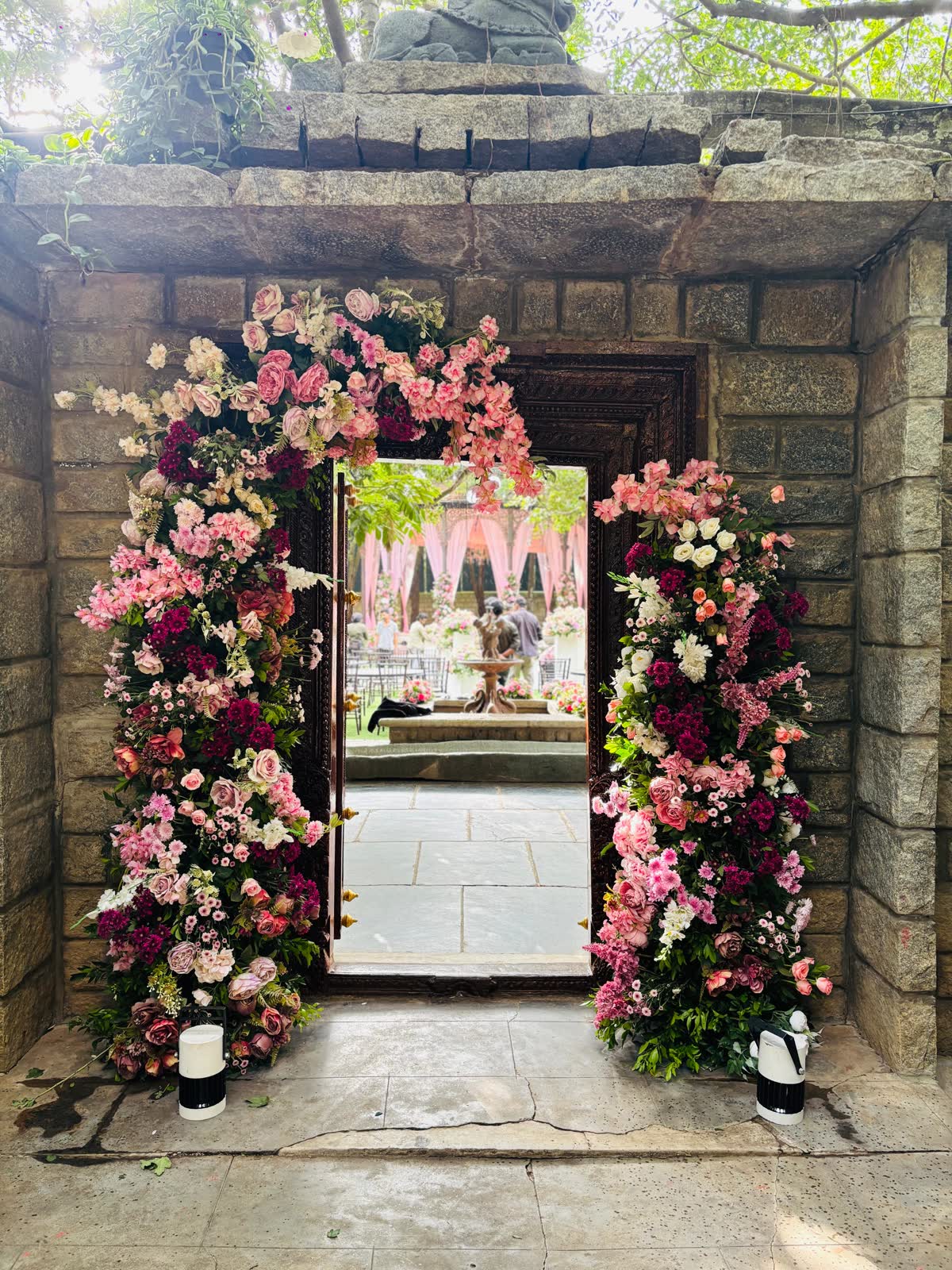 Stone doorway at The Tamarind Tree framed in pink, blush and burgundy roses and chrysanthemum, looking through to the draped reception gazebo beyond