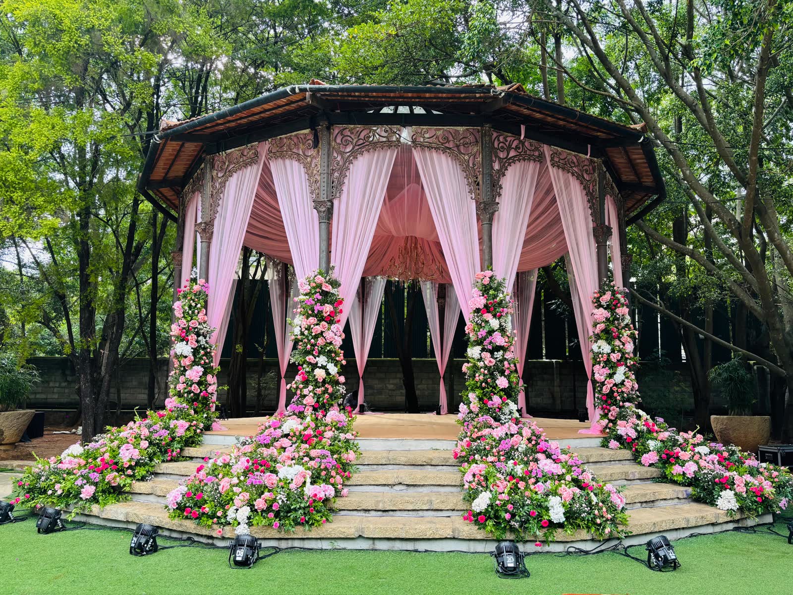 The colonial Gazebo at The Tamarind Tree draped in blush fabric with pink, fuchsia and white floral columns spilling down the stone steps onto the lawn
