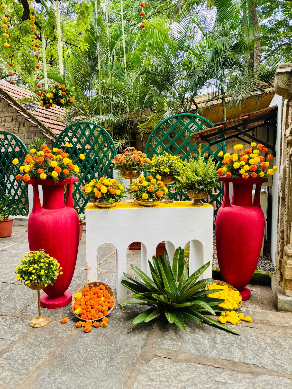 The same white arched console and crimson urns of marigold seen against the green trellis screens and palms at The Tamarind Tree