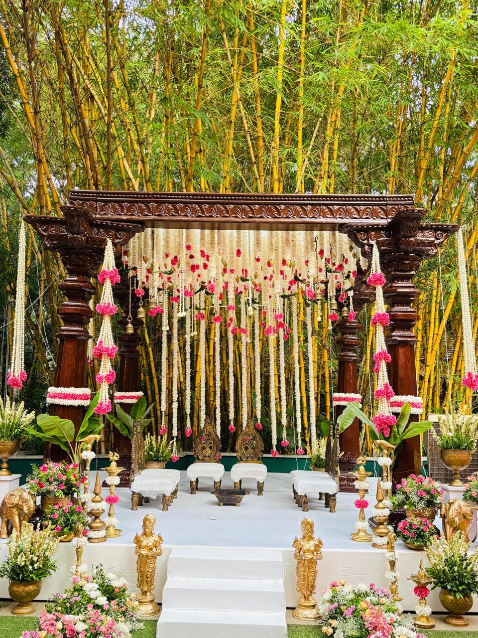 South Indian muhurtham mandap with carved pillars, jasmine garland curtain and pink carnation clusters against bamboo at MG Magnus Bangalore