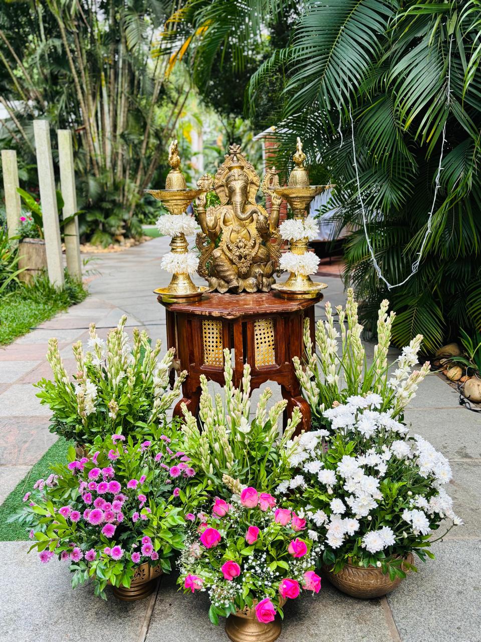 Brass Ganesha on a carved stool with garlanded brass lamps and tuberose arrangements on the entrance path at MG Magnus Bangalore