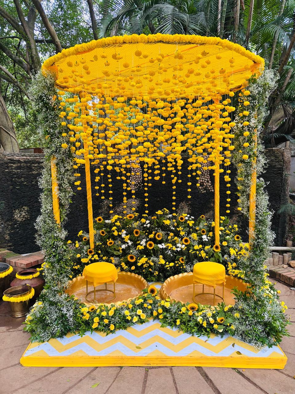 Haldi mandap with circular marigold chandelier canopy, sunflower beds, gold urli basins and chevron platform at MG Magnus Bangalore