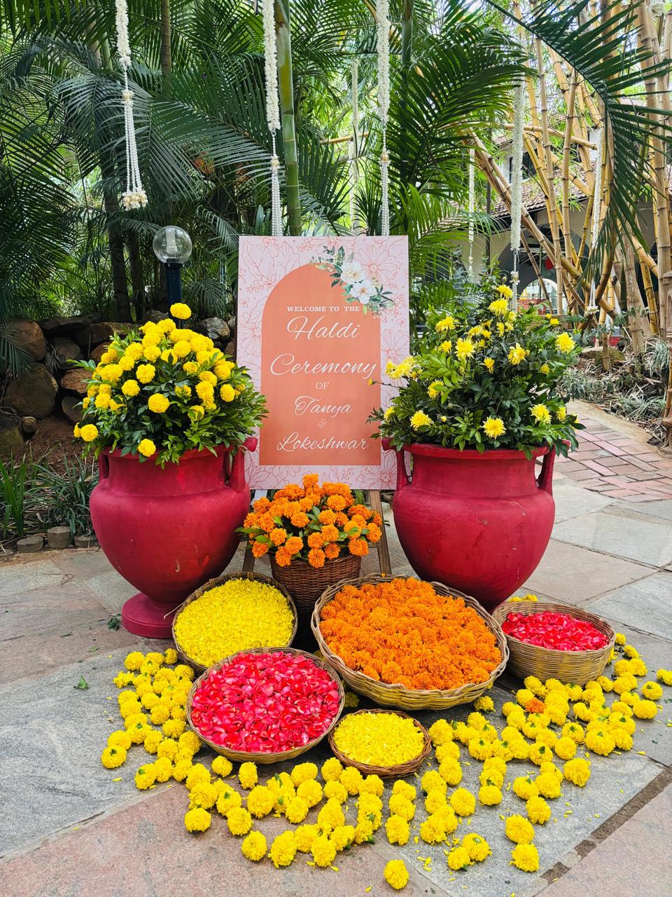 Haldi ceremony welcome board with red urns of marigold and baskets of loose rose and marigold petals at MG Magnus Bangalore
