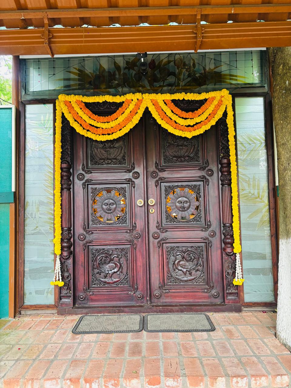 Carved wooden doors with a double-swag marigold toran at the entrance of MG Magnus Miraya Greens Bangalore