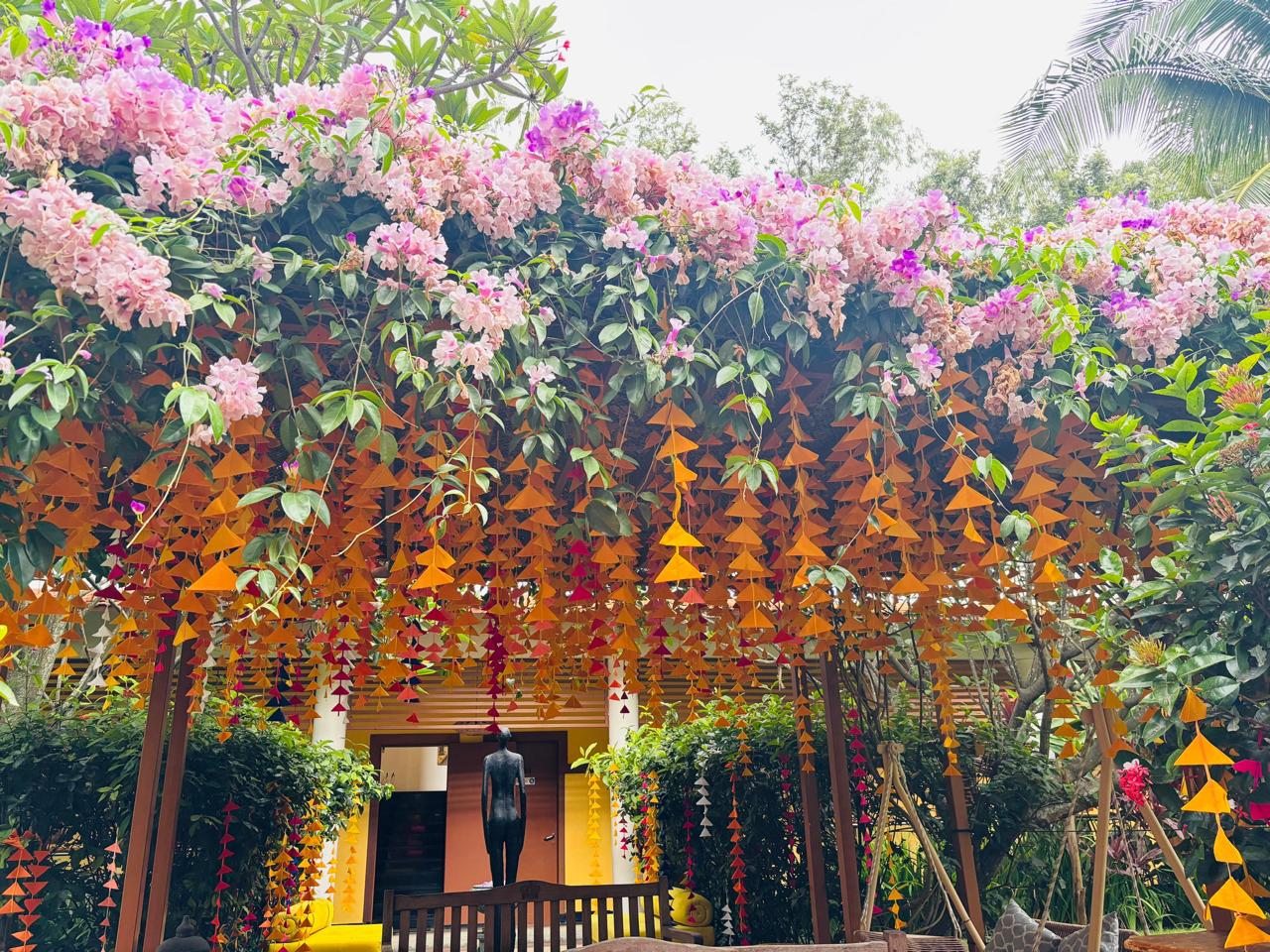 Orange felt bunting strings hanging under a pink bougainvillea canopy at a mehendi at MG Magnus Bangalore