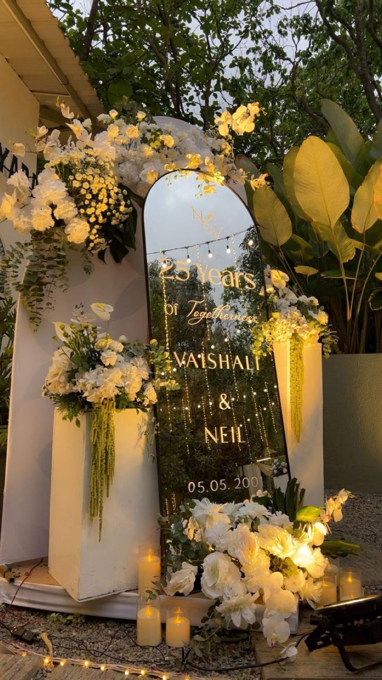Mirrored arch signage reading twenty-five years of togetherness with the couple names and wedding date, framed in ivory florals and candles