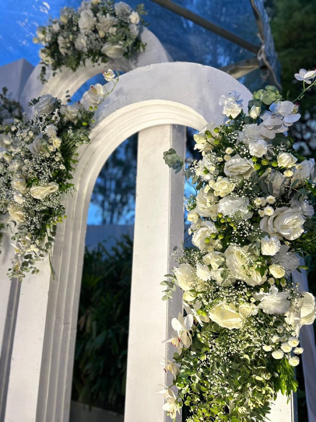 White arched structures with ivory rose and orchid florals photographed against a dusk sky at a Bangalore anniversary