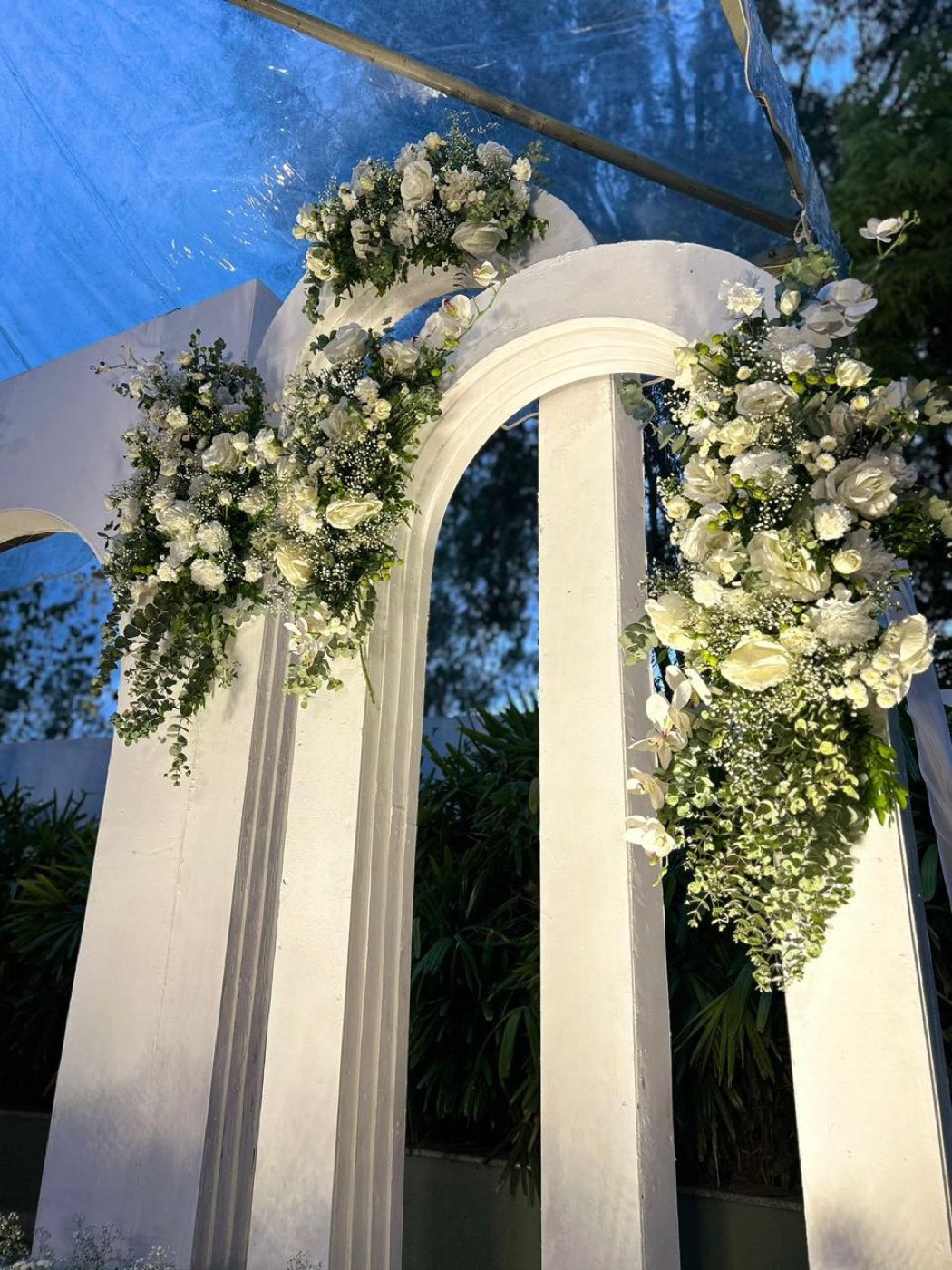 Close detail of white roses, orchids, gypsophila and eucalyptus massed on the shoulder of a white arch